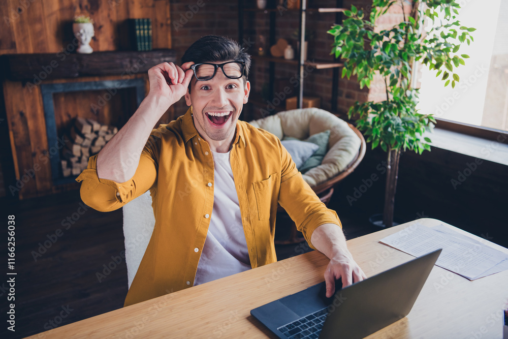 Poster excited young man in casual style enjoying a relaxing day at home indoors, smiling while using a lap