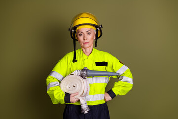 Confident mature woman dressed as a firefighter standing on a khaki background, wearing safety gear...