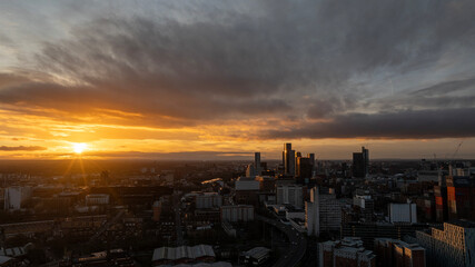 An impressive view of skyscrapers reflecting sunlight under dramatic clouds, emphasizing the interplay between urban architecture and the natural environment.