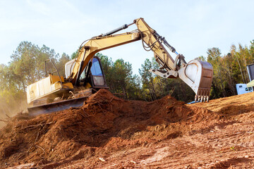 Large excavator works diligently, moving earth, debris at during construction site surrounded...