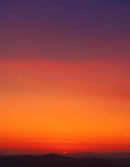 Fototapeta premium Fiery Sunset Landscape Vivid Orange and Purple Sky Over Silhouette Mountains at Dusk