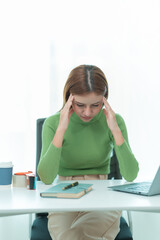 An Asian woman wearing green is tired and has a headache while working at the computer with many...