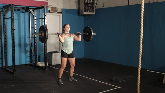 Young female weight lifter lifting barbell from floor over her head.