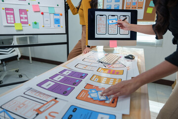 Two web designers are comparing printed and digital versions of user interfaces for mobile apps,...