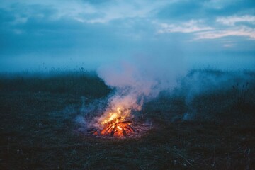 Serene Campfire Flames in Misty Field Under Cloudy Evening Sky