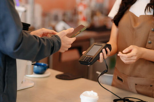 Barista facilitating a contactless payment using a card reader and smartphone. Capturing modern technology