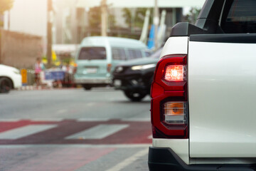 Close up of a white pickup truck taillight. Blurred background shows other vehicles and a pedestrian crossing suggesting an urban traffic scene. © thongchainak