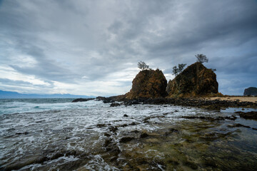 Dramatic coastal scene of Diguisit, Aurora featuring rugged rock formations, under a fast-moving, moody clouds. Calm water reflects the rich tones of the sky, creating a striking and seascape.