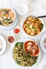Delicious Asian dishes on a dining table. Spicy crispy morning glory salad, spicy clear soup with fresh herbs and stir-fried squid with curry powder.