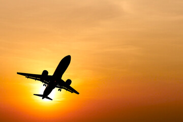 Silhouette of Airplane Taking Off Against Vibrant Orange Sunset Sky with Dramatic Clouds in the Background