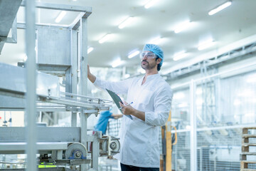 Fototapeta premium An industrial worker wearing a hair cover, gloves, and a lab coat, inspecting machinery and taking notes on a tablet in a modern factory, highlighting precision, safety, and efficiency in operations.