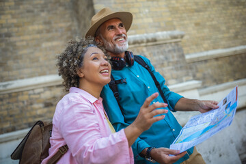 Portrait of happy senior couple tourists outdoors in historic town using map.