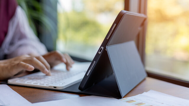 Female hands typing on tablet keyboard on wood desk at office, Technology, Business concept, Business woman analyze the graph of the company performance to create profits and growth. - Powered by Adobe