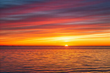 Obraz premium Golden hour sunset illuminating ocean waves crashing on sandy sea beach with colorful cloud sky