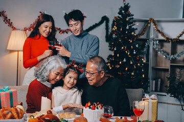 Multi-Generation Family Celebrate Christmas At Home Wearing Santa Hats And Antlers Opening Presents