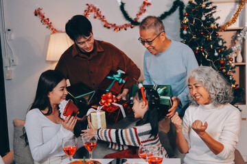 Portrait of Asian family exchanging presents during christmas at home. Attractive happy people holding gift box, celebrate holiday thanksgiving, xmas eve tradition in living room in house together.