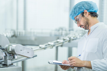 Obraz premium A food processing supervisor wearing protective gear and holding a clipboard, inspecting machinery on a production line, emphasizing quality control, safety, and efficiency in industrial operations.
