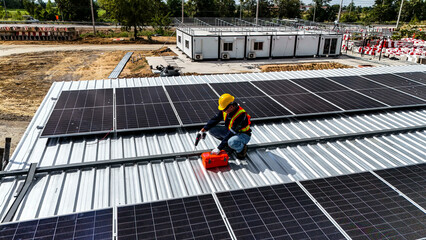 Naklejka premium A worker wearing safety gear installing solar panels on a rooftop with nearby housing units in the background, emphasizing renewable energy, sustainability, and efficient solar power implementation