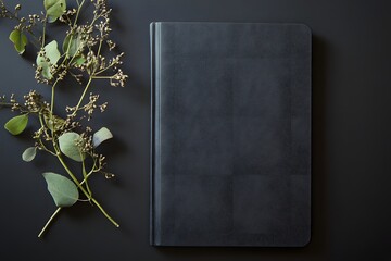Dark gray notebook with eucalyptus branch on dark background.