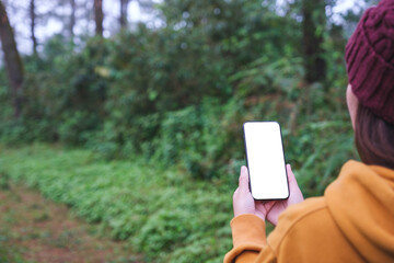 A woman holding mobile phone with blank white desktop screen in the forest