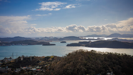It is a beautiful landscape with an emerald sea, many clouds, and many islands.