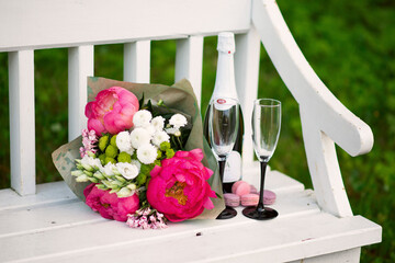 A bouquet of flowers next to a bottle of champagne, two glasses and sweets.