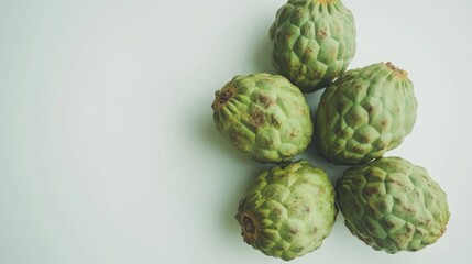 Obraz premium Ripe cherimoya fruits arranged artistically on a light surface showcasing their unique textured skin and vibrant green color.