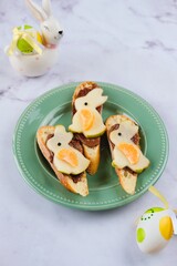 Sweet Easter sandwiches with chocolate spread and pear bunny decoration on green plate on light marble background. Easter dishes, decor.