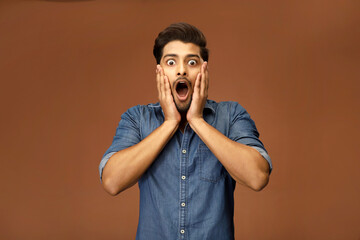 Surprised handsome man keeping his hands on his face.