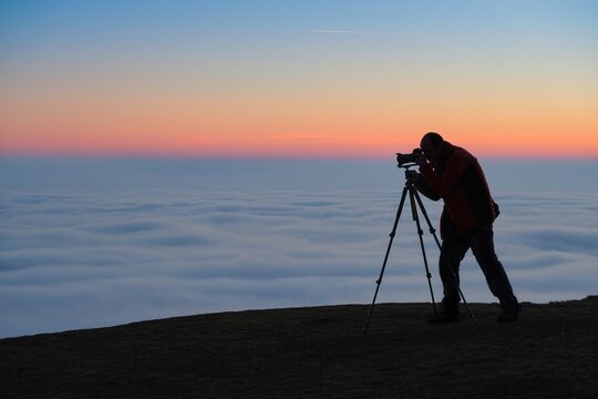 Silhouette of a photographer on a hill with an inversion at sunset. Nature and mountain photography
