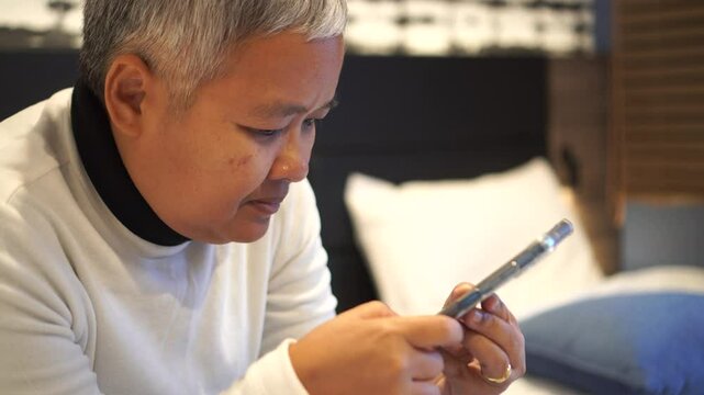 Senior smart chatting in Video call to family in New normal life in bedroom, Reading social media internet and typing text or shopping online with smartphone mobile.