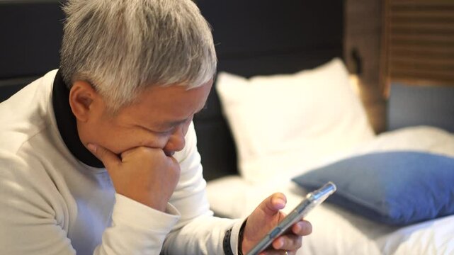 Senior smart chatting in Video call to family in New normal life in bedroom, Reading social media internet and typing text or shopping online with smartphone mobile.