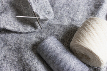 Grey melange knitting sweater with knitting needles. Mix of grey wool and white cashmere with needles. Knitting pattern background. Knitting lifestyle. Cozy hobby. Warm knitwear. Craft product concept