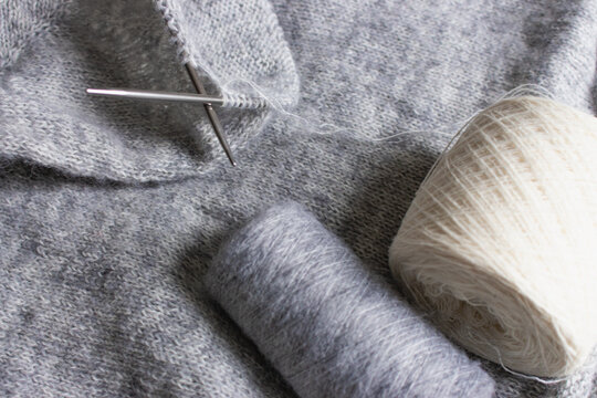 Grey melange knitting sweater with knitting needles. Mix of grey wool and white cashmere with needles. Knitting pattern background. Knitting lifestyle. Cozy hobby. Warm knitwear. Craft product concept