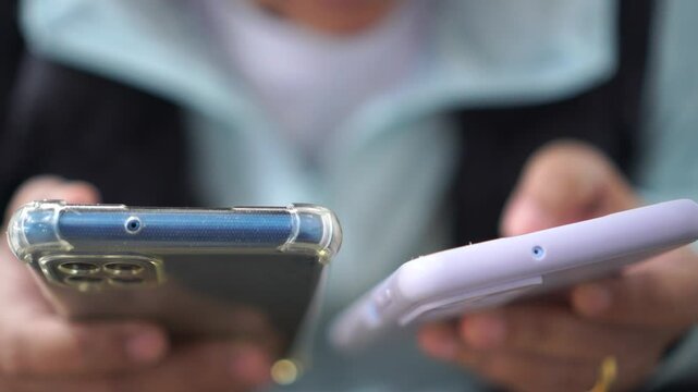 close up hand holding phone, Senior Asian Using two smartphone for scan application technology and money transfer. Touching gadget choose app on mobile phone