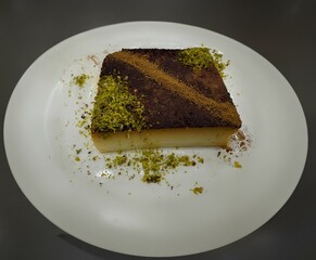 Kazandibi dessert. Kazandibi dessert is a type of Turkish dessert in a white plate on an isolated black background. Kazandibi dessert decorated with pistachios and cinnamon.
