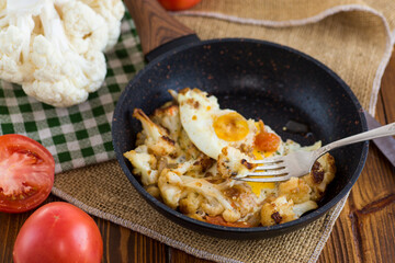 fried omelette with cauliflower and vegetables in a frying pan on a wooden table