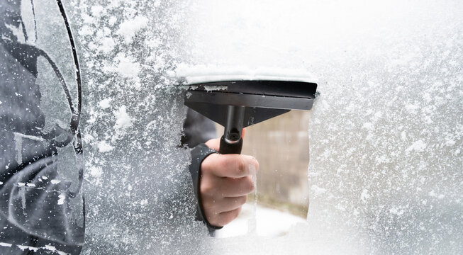 Driver is removing snow from car windshield with ice scraper and broom, clean car window from icy frost, winter season