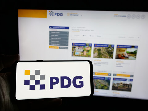 Stuttgart, Germany - 12-19-2024: Person holding smartphone with logo of Brazilian real estate company PDG Realty SA on screen in front of website. Focus on phone display.