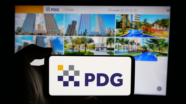 Stuttgart, Germany - 12-19-2024: Person holding cellphone with logo of Brazilian real estate company PDG Realty SA on screen in front of business webpage. Focus on phone display.
