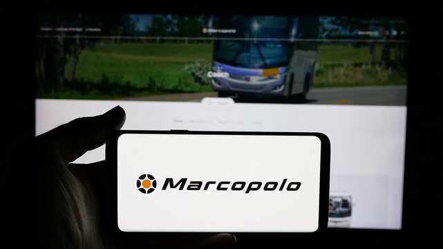 Stuttgart, Germany - 12-19-2024: Person holding cellphone with logo of Brazilian automotive company Marcopolo SA on screen in front of business webpage. Focus on phone display.