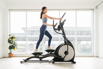 Fototapeta premium A fit woman exercises on an elliptical machine in a bright, modern indoor space, promoting health and fitness.