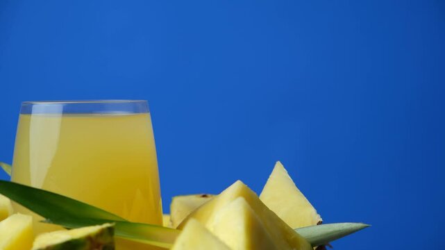 Spinning a glass of pineapple juice among fresh pineapples, blue background, space for text