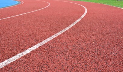 Fototapeta premium red running track curve with white lines and green grass in right side