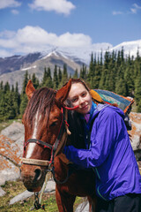 A young girl hugs a horse 's head and holds the reins. A rider and a horse in the mountains against...