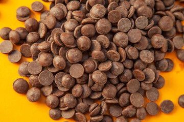 Chocolate chips closeup on a yellow background, big chunks.