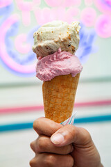 Double scoop strawberry and vanilla gelato ice cream waffle cone holding by male hand.
