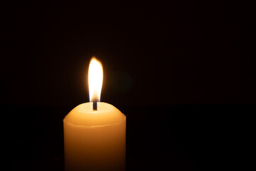 A single burning candle flame or light glowing on a big white candle isolated on red or dark background on table in church for Christmas, funeral or memorial service