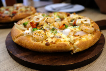 A vegetarian pizza and a seafood pizza are on a wooden table in a pizzeria