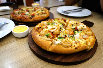 A vegetarian pizza and a seafood pizza are on a wooden table in a pizzeria